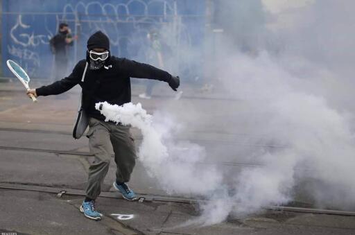 protester hitting a canister with a tennis racket
