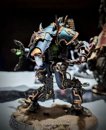 War-Dog Moirax miniature from Games Workshop armed with a Siege Claw and Conversion Beamer. The model has dark turquoise armor with dirty bronze trim and its exhaust vents glow green with leaking radiation. A nameplate on the model's base reads "Vixen".