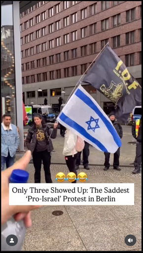 image: woman holding flagstaff with the flag of Israel below that of the IDF. Next to her stands a man in a light blue jacket. Partially obscured by one of the flags stands another man.
text:
Only Three Showed Up: The Saddest 'Pro-Israel' Protest in Berlin
