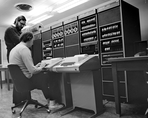 black and white photograph of two people in front of a DEC PDP-11 computer. see post body for detailed description