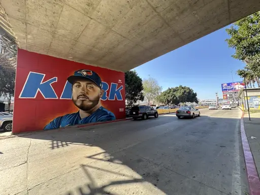 Picture of a painted Alejandro Kirk mural on the wall of a highway underpass. There's a headshot of Kirk wearing a Blue Jays cap, his last name in large letter behind his head, all against a red background. I'd guess that this is in Mexico.